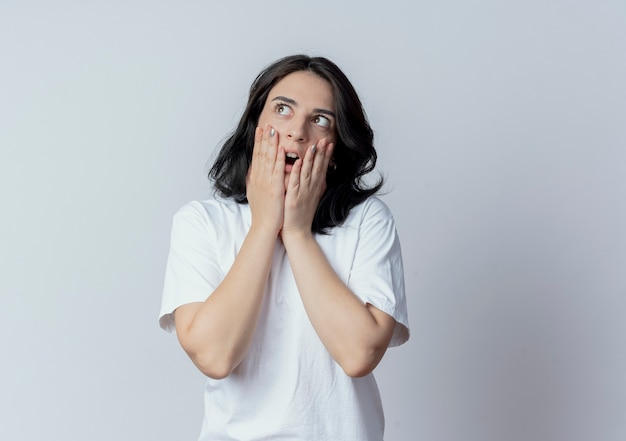 Surprised young pretty caucasian girl looking at side and putting hands on face isolated on white background with copy space