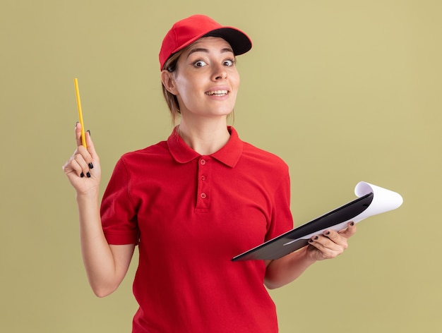 Foto gratuita la giovane donna graziosa sorpresa di consegna in uniforme tiene la matita ed i appunti isolati