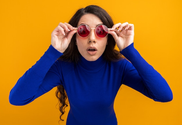 Surprised young pretty girl wearing sunglasses grabbing glasses