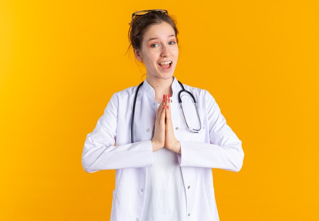 Удивленная молодая славянская девушка в униформе врача со стетоскопом, изолированной на оранжевой стене с копией пространства