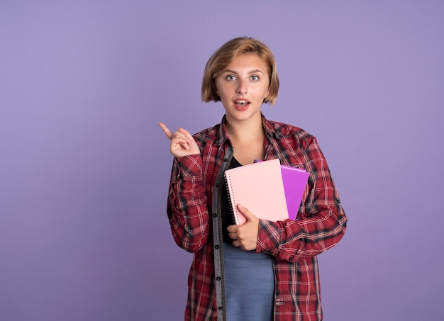 驚いた若いスラブ学生の女の子が本とノートのポイントを横に持っている