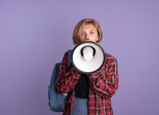 Surprised young slavic student girl wearing backpack speaks into loud speaker 