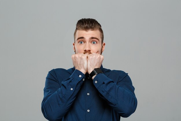 Surprised young successful businessman posing over grey wall.