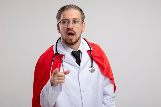 Free photo surprised young superhero guy looking at side wearing medical robe with stethoscope and glasses