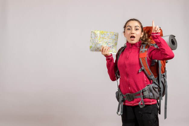 surprised young traveller with big backpack holding up map pointing finger up