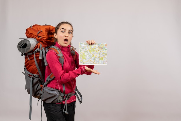 Surprised young traveller with big red backpack holding map on grey isolated