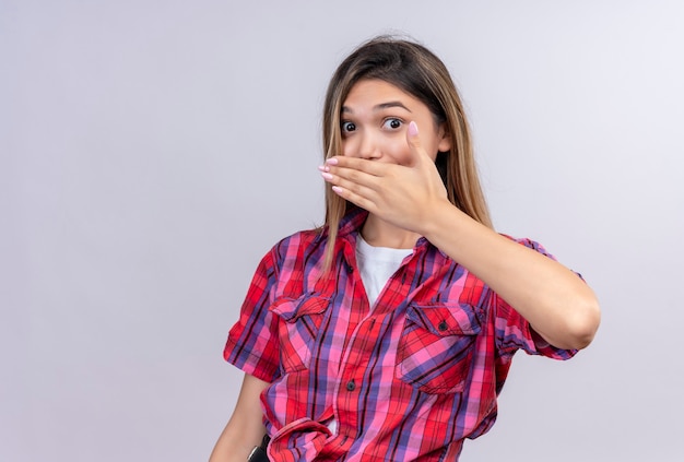 A surprised young woman in a checked shirt keeping hand on mouth