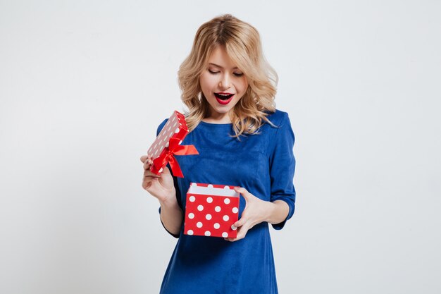 Surprised young woman holding gift box over white wall