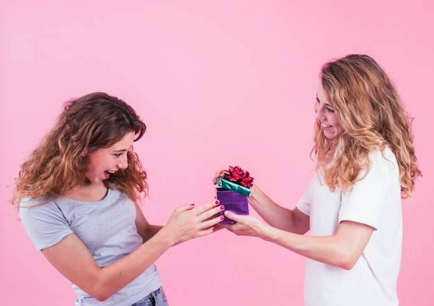 Free photo surprised young woman looking at gift box hold by her friend