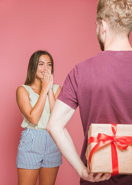 Surprised young woman looking at her boyfriend hiding gift box