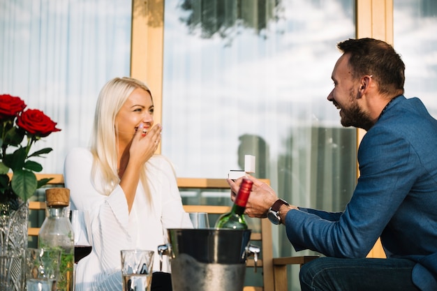 Surprised young woman looking at man giving engagement ring in restaurant