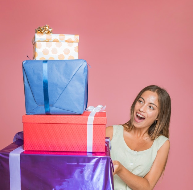 Удивленная молодая женщина, глядя на стек подарочной коробке на цветном фоне