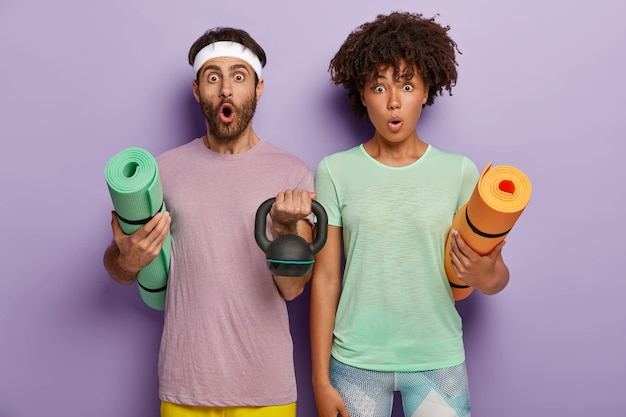 Free photo surprised young woman and man carry karemats, lift weight, dressed in sportwear