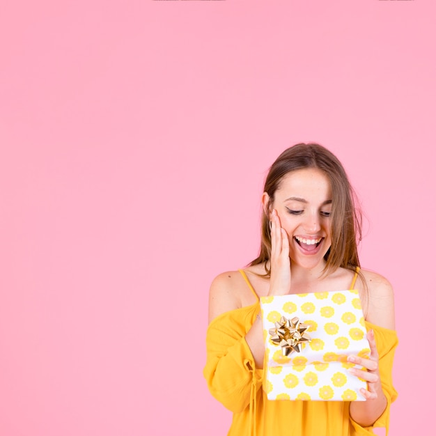 Foto gratuita giovane donna sorpresa che apre la scatola del presente del pois giallo con l'arco dorato