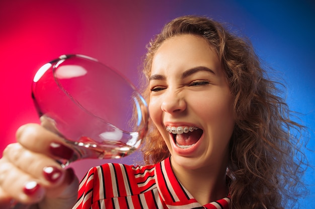 surprised young woman in party clothes posing with glass of wine. Emotional female cute face. View from the glass