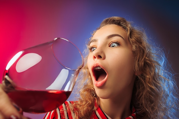 surprised young woman in party clothes posing with glass of wine. Emotional female cute face. View from the glass