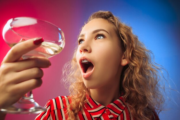 surprised young woman in party clothes posing with glass of wine. Emotional female cute face.