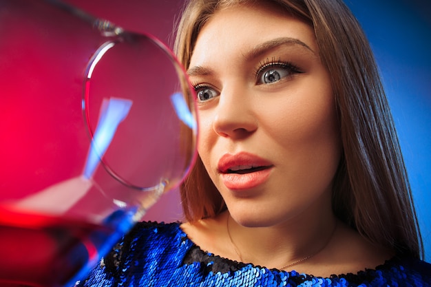 Free photo the surprised young woman in party clothes posing with glass of wine