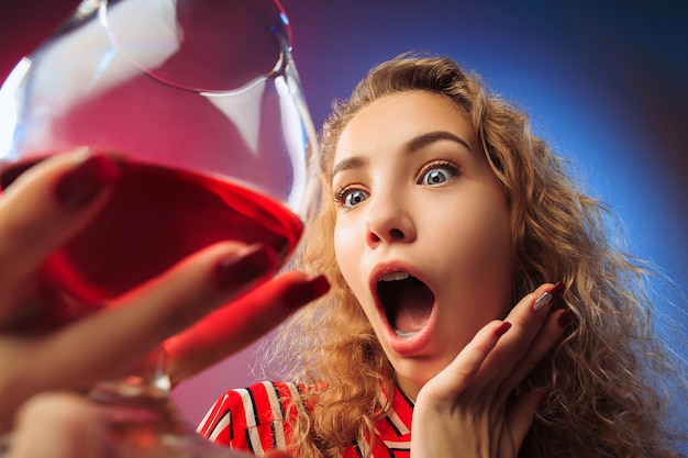 Free photo the surprised young woman in party clothes posing with glass of wine