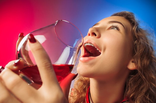 Удивленная молодая женщина в праздничной одежде позирует с бокалом вина.