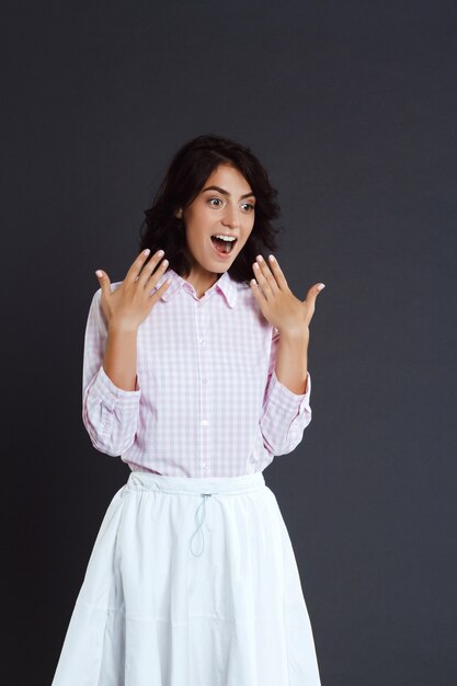 Surprised young woman posing over grey wall