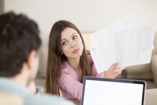 Free photo surprised young woman showing papers to man with questioning loo