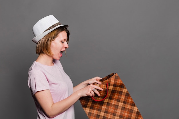 Surprised young woman wearing hat looking inside the shopping bag