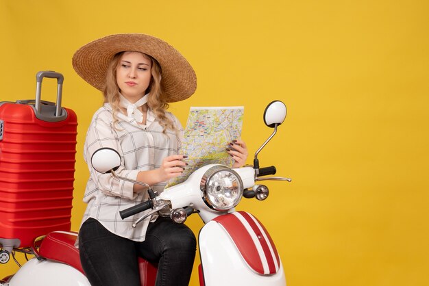 Удивленная молодая женщина в шляпе, сидящая на мотоцикле и держащая карту на желтом