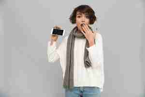 Free photo surprised young woman wearing scarf showing display of mobile phone.