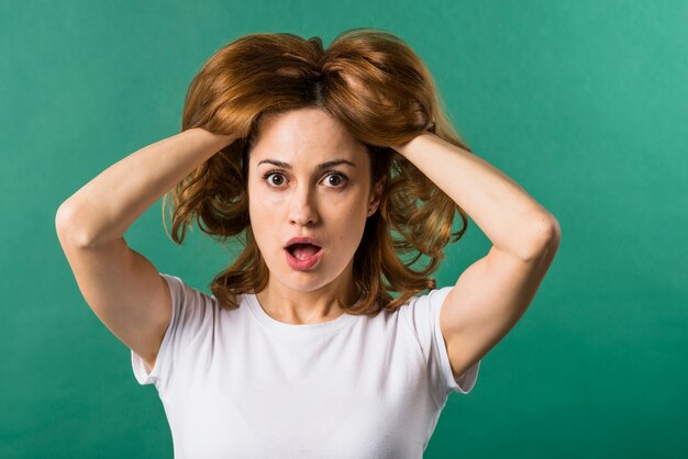 Surprised young woman with her two hands in hair against green backdrop