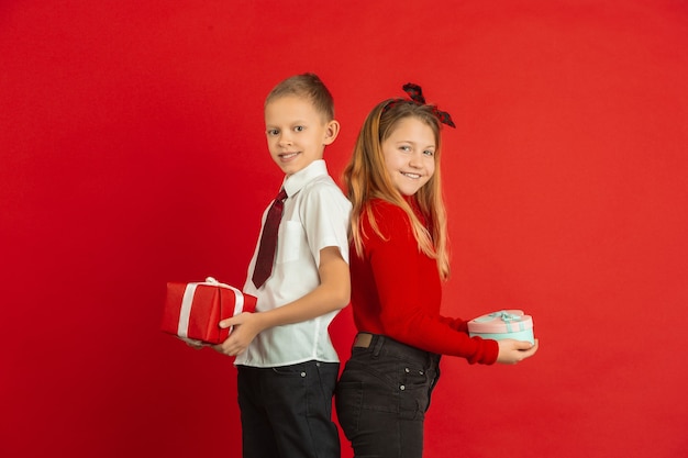 Surprising moment. Valentine's day celebration, happy, cute caucasian kids isolated on red studio background. Concept of human emotions, facial expression, love, relations, romantic holidays.