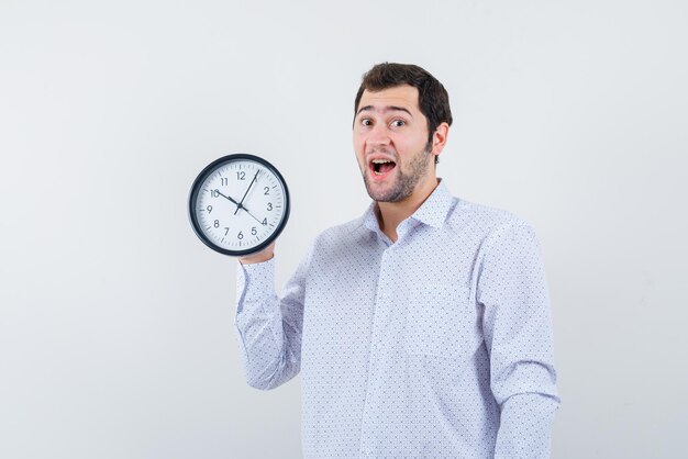 Surprising young man holding an oclock on his hand on white background