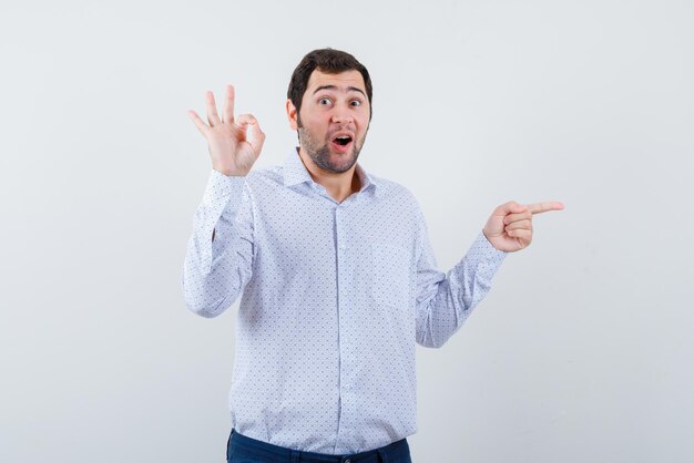 Surprising young man showing a good hand gesture and pointing something with fingers on the right on white background