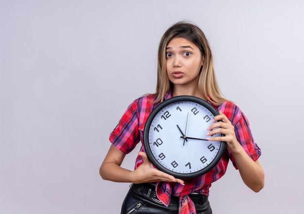 A surprising young woman in checked shirt holding wall clock