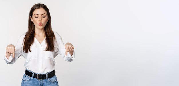 Surprsed businesswoman beautiful adult woman pointing fingers down looking excited at camera standing over white background