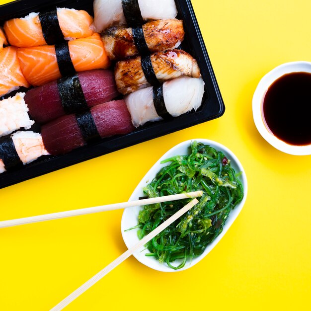 Sushi box plate with seaweed salad and soy sauce on yellow background