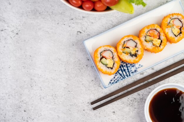 Sushi is in a plate with chopsticks and dipping sauce on a white cement floor.