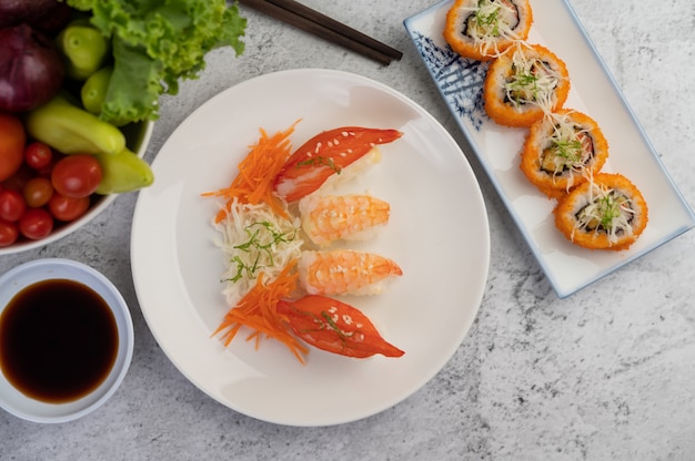 Sushi is in a plate with chopsticks and dipping sauce on a white cement floor.