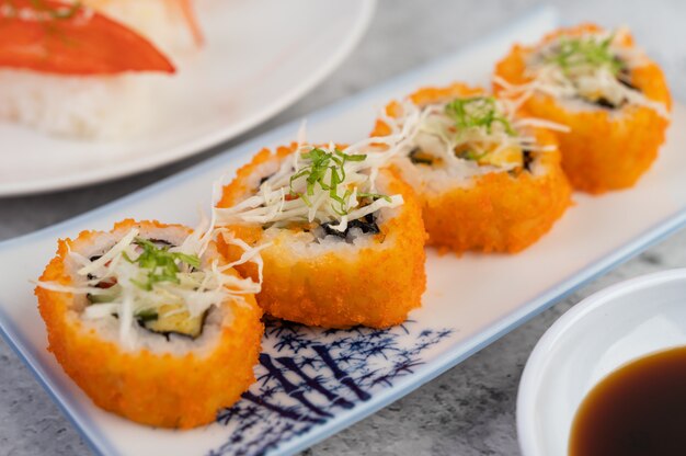 Sushi is on a plate with dipping sauce on a white cement floor.