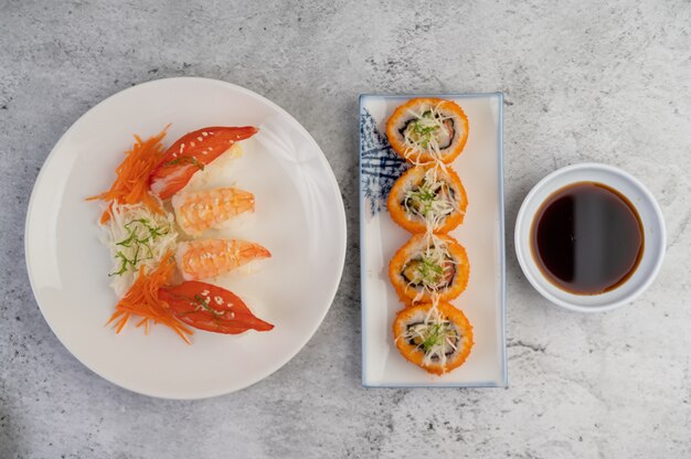 Sushi is on a plate with dipping sauce on a white cement floor.