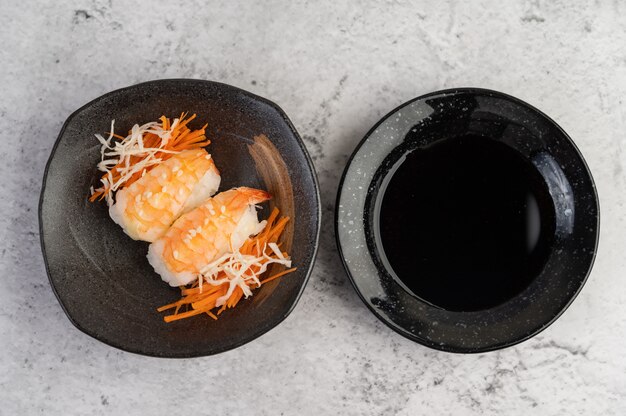 Sushi is on a plate with dipping sauce on a white cement floor.