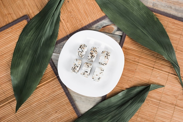 Sushi roll on white plate with green leaves and placemat