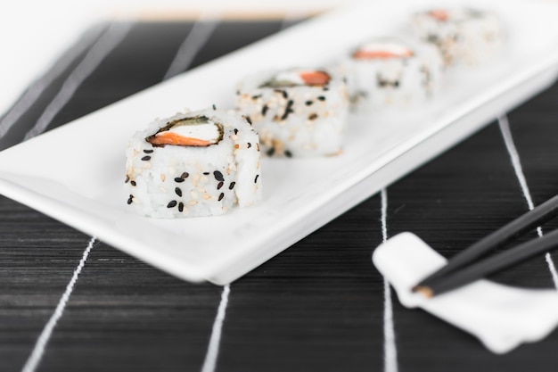 Sushi roll on white tray with chopsticks