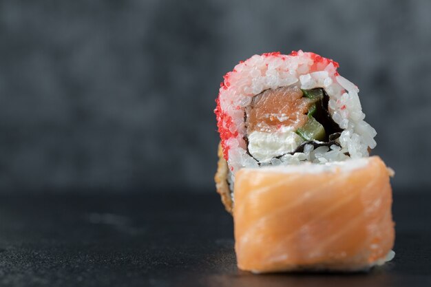 Sushi roll with mixed ingredients isolated on black table.