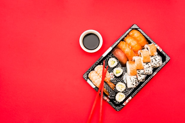 Sushi rolls and sashimi on tray with soy sauce over colored background