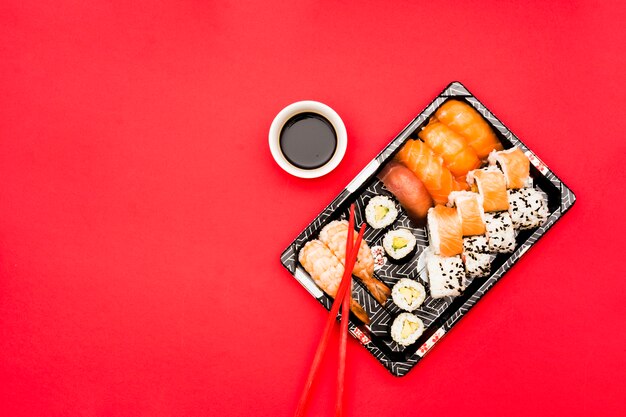 Sushi rolls and sashimi on tray with soy sauce over colored background