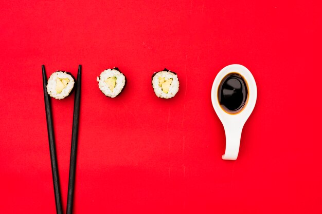 Sushi rolls with chopsticks and soya sauce over red background