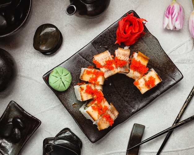 赤い生ingerとわさびを添えた黒い石の板にパプリカを巻いた寿司。