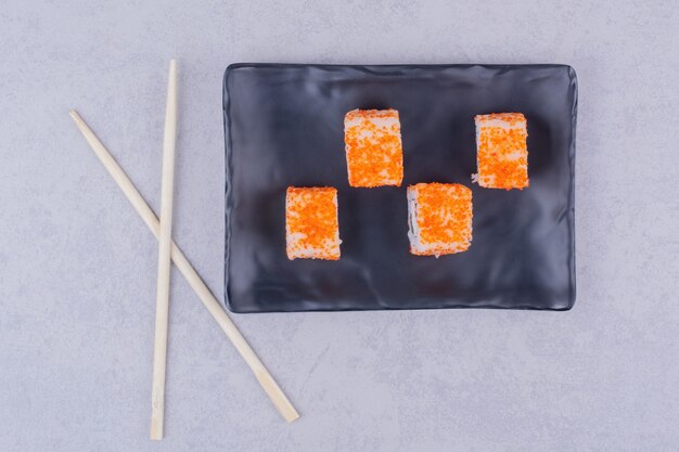 Sushi rolls with salmon in a black ceramic platter.