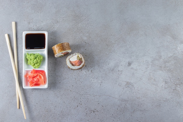 Суши-роллы с соевым соусом кладут на белую доску палочками для еды.